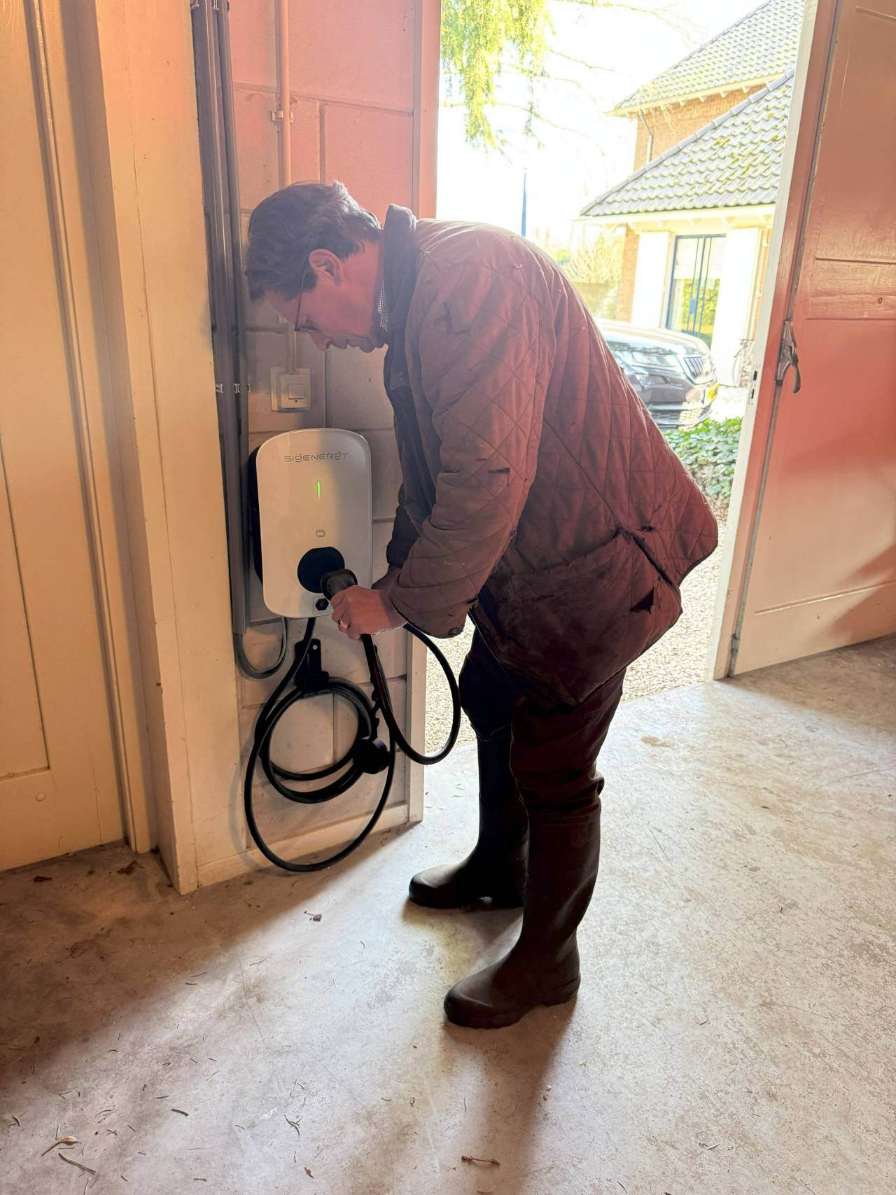 Tevreden klant Beter Duurzaam doet stekker in laadpaal Sigenergy in zijn schuur nadat hij auto heeft opgeladen